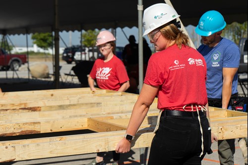 two Fort Wayne Metals employees help a Habitat for Humanity employee carry part of a framed wooden wall